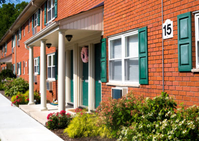 Exterior of brick apartment building on sunny day with lots of windows and landscaping