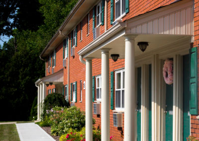 Exterior of brick apartment building with green shutters and and white pillars outside of green front door