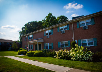 Exterior brick apartment building with green shutters and beautifully landscaped grounds