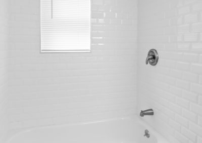 Bathroom tub and shower with white tile walls and small window with blinds