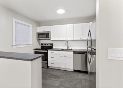 Open kitchen concept with white cabinets, stainless steel appliances, on vinyl flooring.