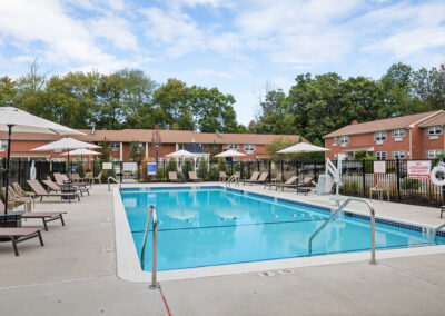 Community pool and pool house surrounded by reclining chairs and umbrellas for shade.