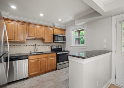 Open kitchen with wooden cabinets, white walls, stainless steel appliances on vinyl flooring.