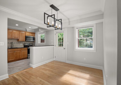 Living room facing the open kitchen with a lighting chandelier over the living room near the main entrance and window on hardwood-style flooring