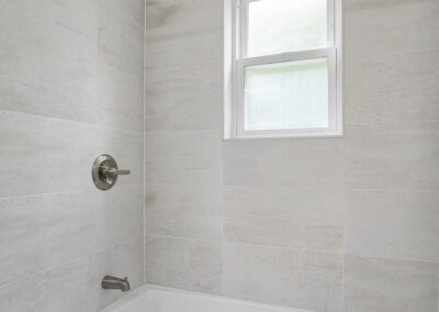 Bathroom tub and shower with white tile walls and small window with blinds
