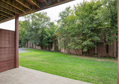 Apartment patio with grass and tree's next to a large fence